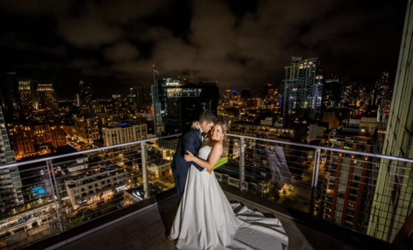 Loving couple embracing on a rooftop in San Diego, surrounded by a vibrant cityscape illuminated by night lights
