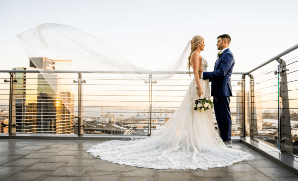Romantic couple sharing a moment on a rooftop wedding venue, with the bride's veil flowing in the wind and the sunset reflecting off city skyscrapers
